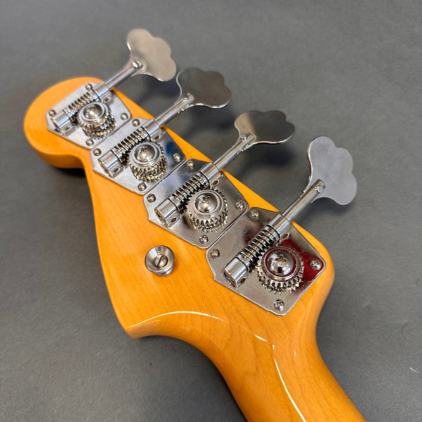 Close-up of vintage-style chrome tuning pegs on natural wood bass guitar headstock against gray background