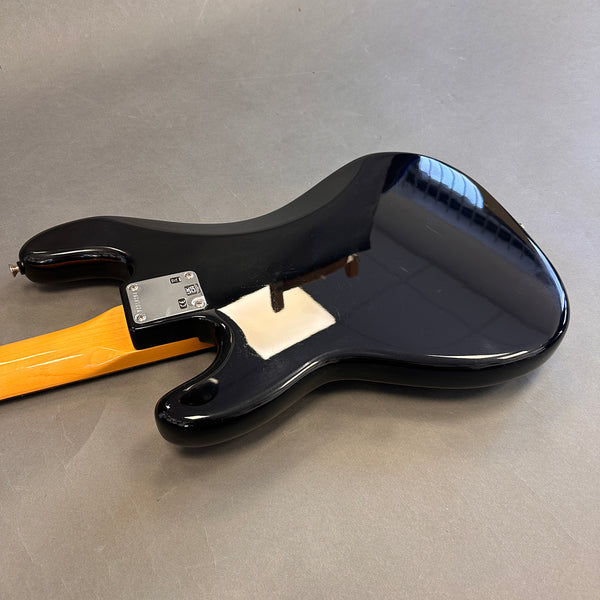 Black electric guitar body with maple neck and metal neck plate on gray surface, rear view showing guitar back and heel.