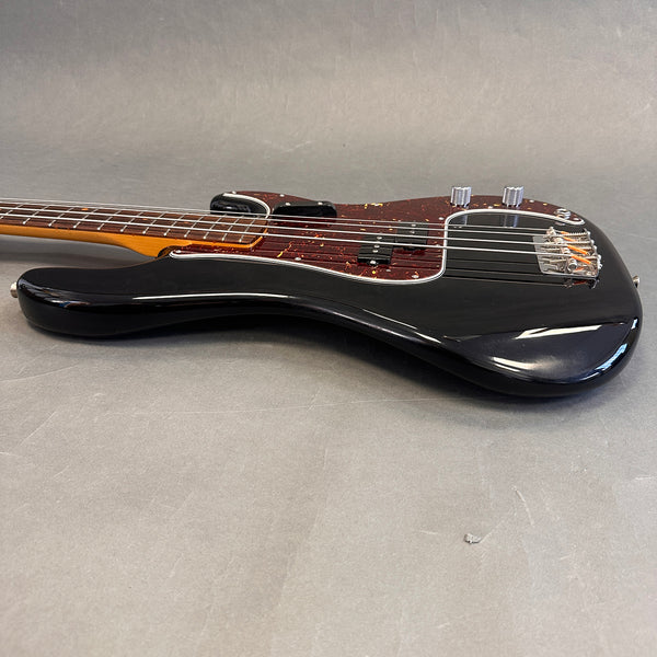 Black electric bass guitar with tortoiseshell pickguard and chrome hardware on gray background