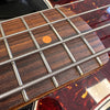 Close-up of bass guitar fretboard with metal frets, round orange inlay, and tortoiseshell pickguard detail