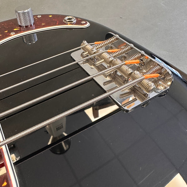 Close-up of black electric bass guitar bridge with metal saddles and wound steel strings at Coffee House Guitars