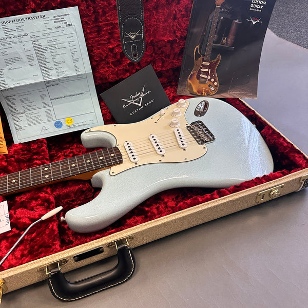 Fender electric guitar in silver sparkle finish with white pickguard and rosewood fretboard inside a tan hardshell case with red plush interior, accompanied by custom care booklet and guitar specification sheet.