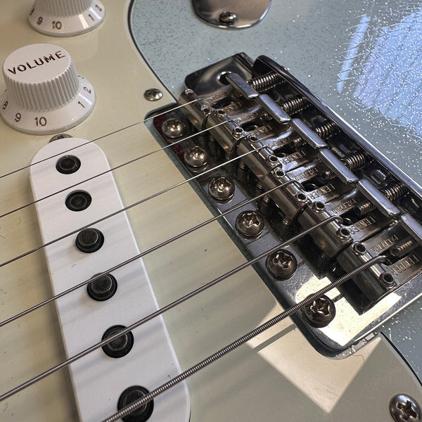 Close-up of electric guitar bridge, strings, white pickup, and volume control knob with vintage-style detailing