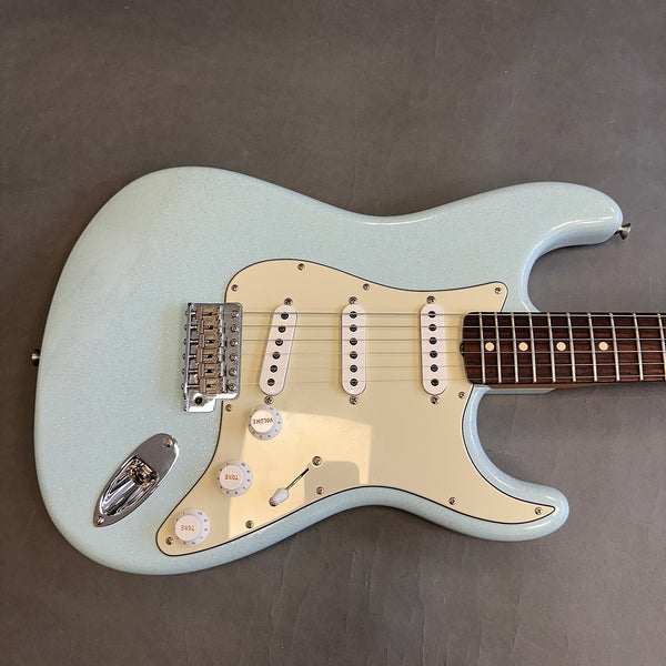 Light blue electric guitar with three single-coil pickups, cream pickguard, white control knobs, and rosewood fingerboard on grey background
