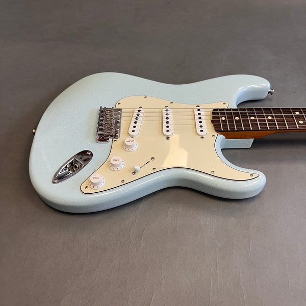 Light blue electric guitar with white pickguard and three single-coil pickups on gray background