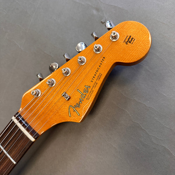Close-up of Fender Stratocaster guitar headstock with tuning pegs and rosewood fretboard on gray background