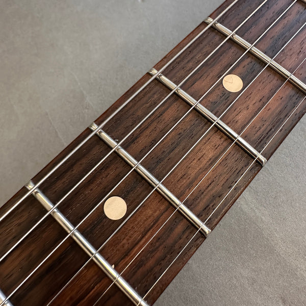 Close-up of acoustic guitar rosewood fretboard with metal frets and dot inlays on a gray background