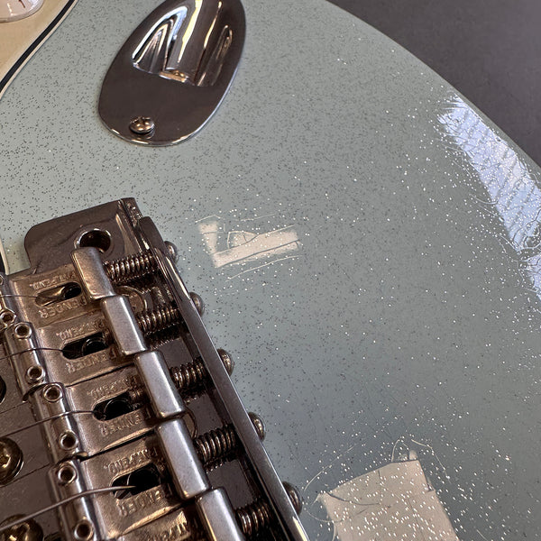 Close-up of vintage Fender electric guitar bridge and sparkly light blue guitar body finish with aging cracks and speckled patina
