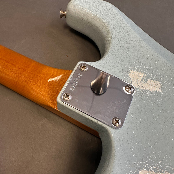 Close-up of guitar neck joint with chrome neck plate and screws on a light blue speckled electric guitar body with a natural wood neck.