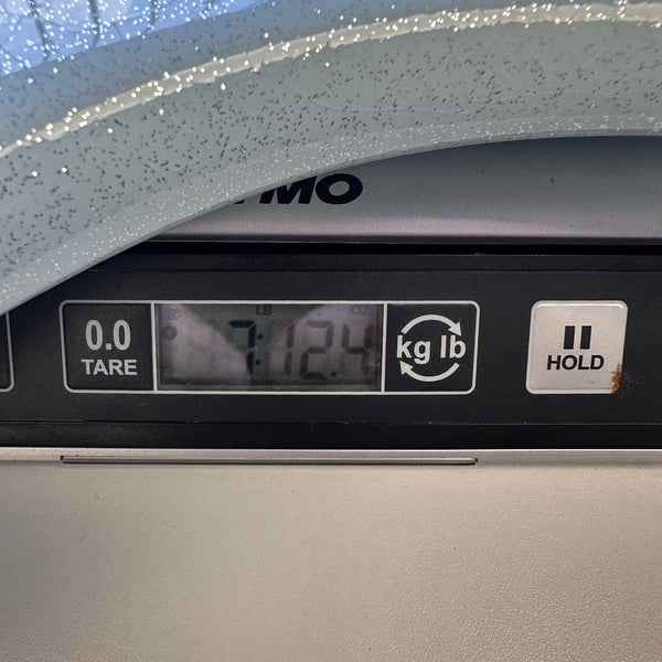 Digital scale close-up showing guitar weight as 7 pounds 12.4 ounces with tare and hold buttons visible