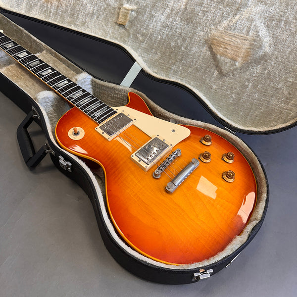 Sunburst electric guitar with humbucker pickups in open hard shell case on gray surface