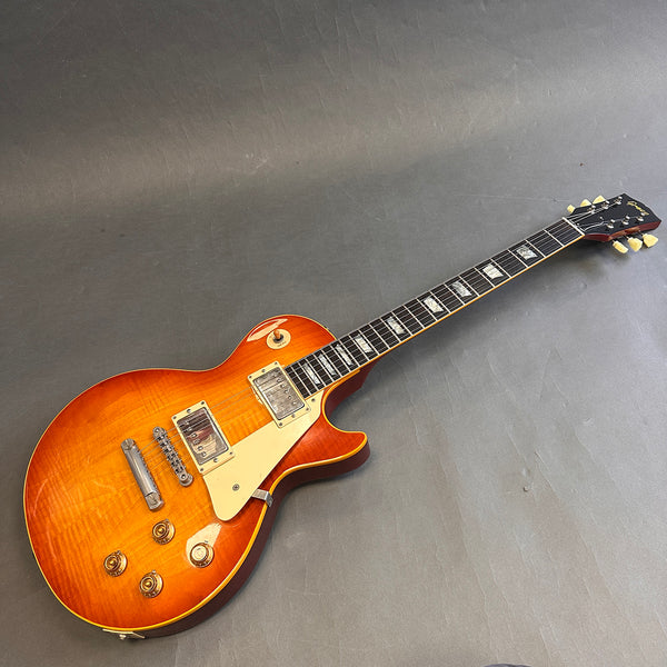 Electric guitar with sunburst finish, dual humbucker pickups, cream pickguard, and trapezoid inlays on ebony fretboard on a gray background