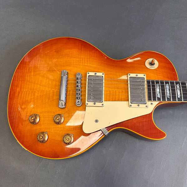 Close-up of sunburst electric guitar body with chrome pickups, cream pickguard, and amber control knobs on gray background