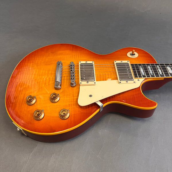 Close-up of a sunburst electric guitar with dual humbucker pickups, cream pickguard, four control knobs, and a toggle switch on a gray background