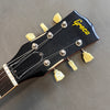Close-up of Greco electric guitar black headstock with yellow tuning pegs and strings attached on gray background