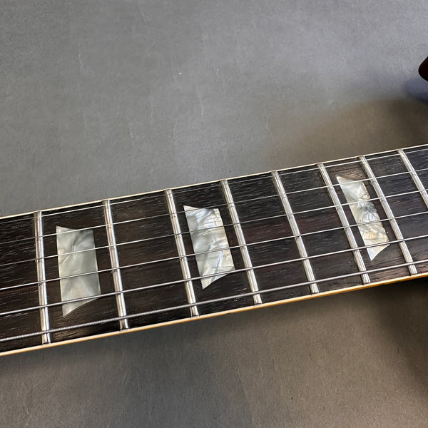 Close-up of electric guitar fretboard with pearl trapezoid inlays and metal frets on dark wood fingerboard