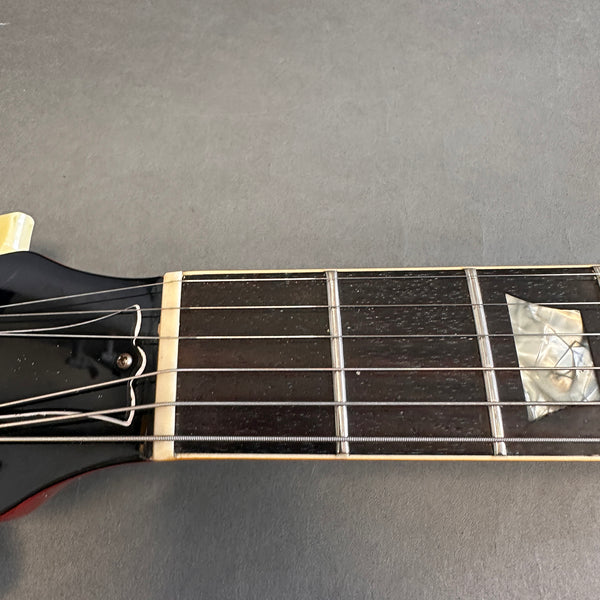 Close-up of black electric guitar headstock and fretboard with pearl inlay on gray surface