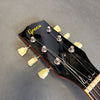 Close-up of black Greco guitar headstock with yellow tuning pegs and strings on gray background