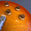 Close-up of amber electric guitar body showing four gold volume and tone control knobs and part of the metallic bridge assembly