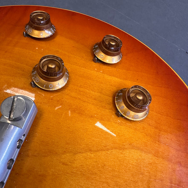 Close-up of amber electric guitar body showing four gold volume and tone control knobs and part of the metallic bridge assembly