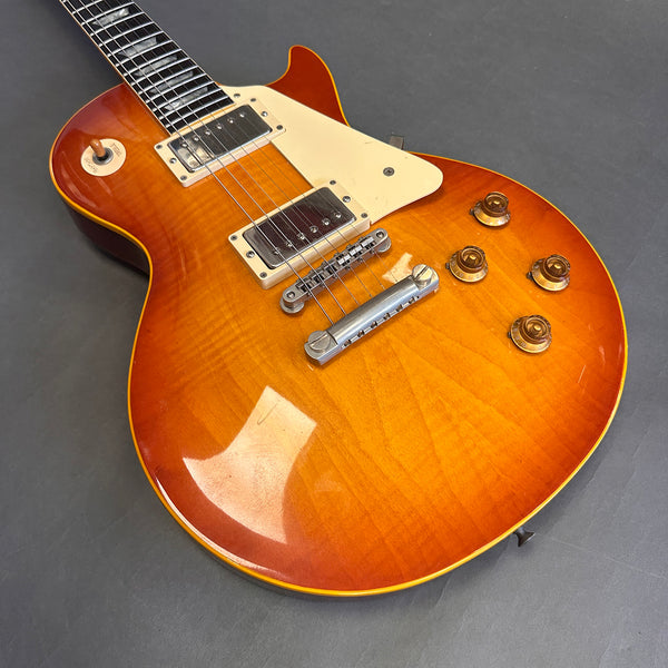 Close-up image of sunburst finish electric guitar body with dual humbucker pickups, cream pickguard, and control knobs on gray background