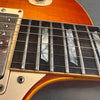 Close-up of electric guitar fretboard with mother-of-pearl inlays, metal frets, and six steel strings on sunburst finish body, showing pickup and switch tip.