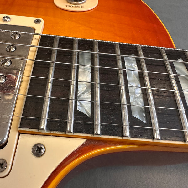 Close-up of electric guitar fretboard with mother-of-pearl inlays, metal frets, and six steel strings on sunburst finish body, showing pickup and switch tip.