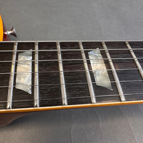Close-up of electric guitar fretboard with pearloid trapezoid inlays and steel strings on dark wood fingerboard