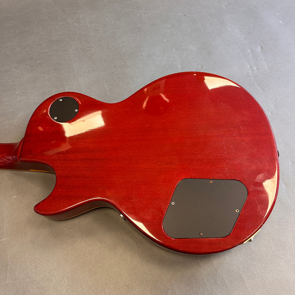 Back of red electric guitar body with two black plastic control cavity covers on gray surface