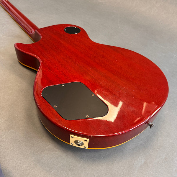 Back view of red electric guitar with black control cavity covers, cream binding, and output jack on gray background