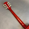 Back view of red guitar neck and headstock with six tuning pegs on gray surface