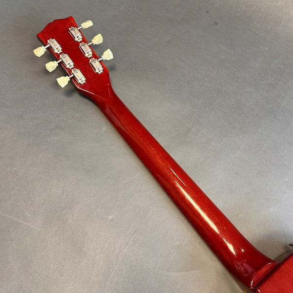 Back view of red guitar neck and headstock with six tuning pegs on gray surface