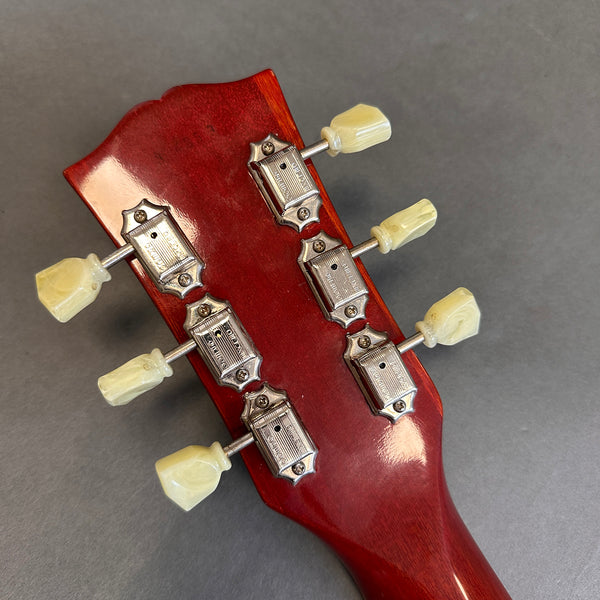 Close-up of vintage red guitar headstock with six white tuning pegs and chrome tuning machines on gray background