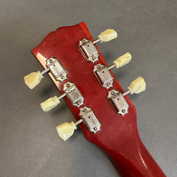 Close-up of red guitar headstock with six vintage Kluson Deluxe tuning pegs and cream plastic tuning keys on gray surface