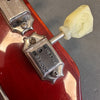 Close-up of vintage guitar tuning peg with cream-colored plastic knob on red guitar headstock with chrome hardware and "Grover" branding.