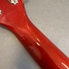 Close-up of glossy red wood guitar neck back and headstock area on gray surface