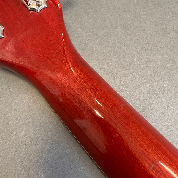 Close-up of glossy red wood guitar neck back and headstock area on gray surface