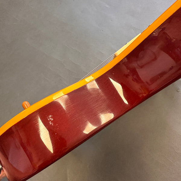 Close-up of glossy reddish-brown guitar body with yellow binding and metal strings on gray background
