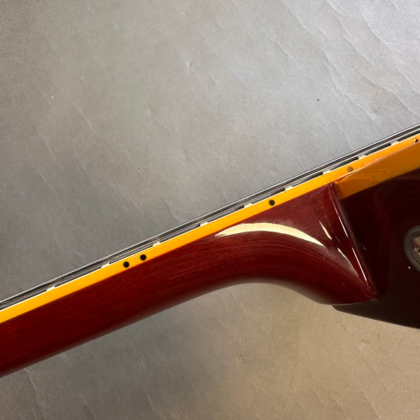 Close-up of guitar neck heel with glossy dark wood finish and cream binding against gray textured background
