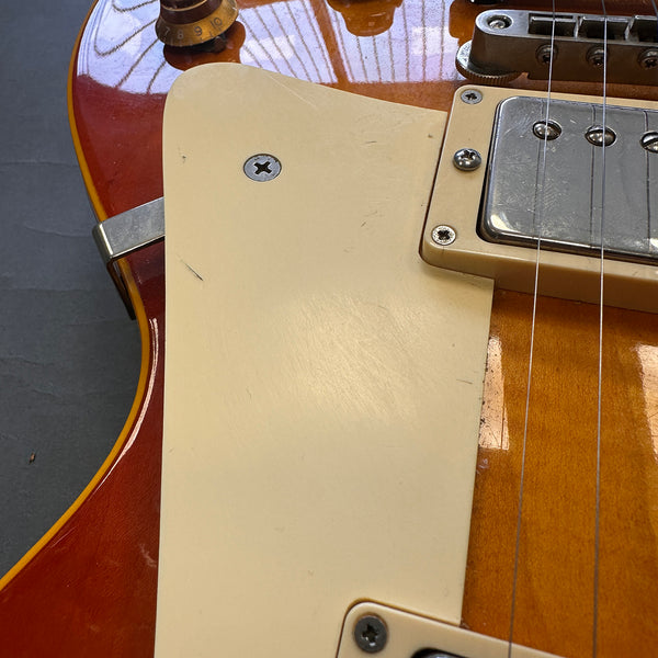 Close-up of vintage sunburst electric guitar body showing cream pickguard, humbucker pickup, and volume knob with wear details