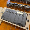 Close-up of electric guitar bridge and chrome humbucker pickup on amber wood finish guitar body