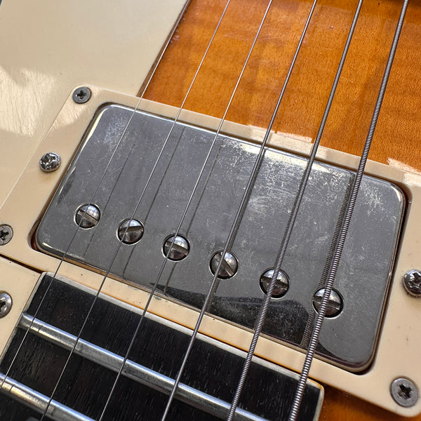 Close-up of electric guitar chrome pickup and strings on wood finish body with cream plastic mounting ring and screws