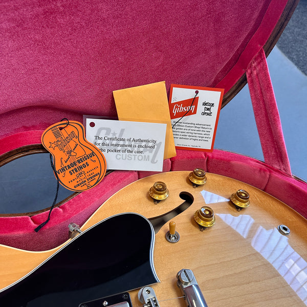Gibson electric guitar with vintage tone circuit tag, certificate of authenticity, and vintage reissue strings label inside a pink velvet-lined guitar case.