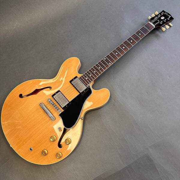 Gibson hollow body electric guitar with natural wood finish, dual humbucker pickups, black pickguard, and rosewood fretboard on gray background