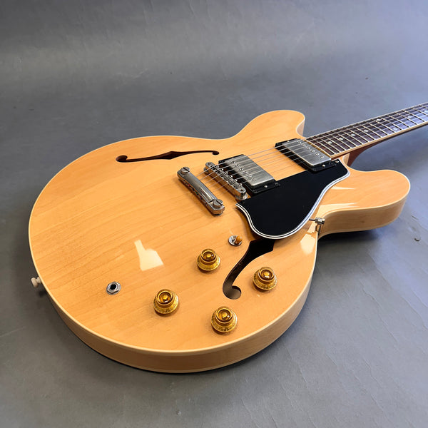Natural finish semi-hollow electric guitar with dual humbucker pickups, black pickguard, and gold control knobs on grey background