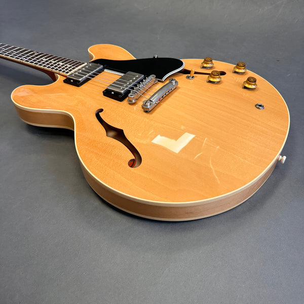 Semi-hollow body electric guitar with natural wood finish, black pickguard, humbucker pickups, and amber control knobs on grey background