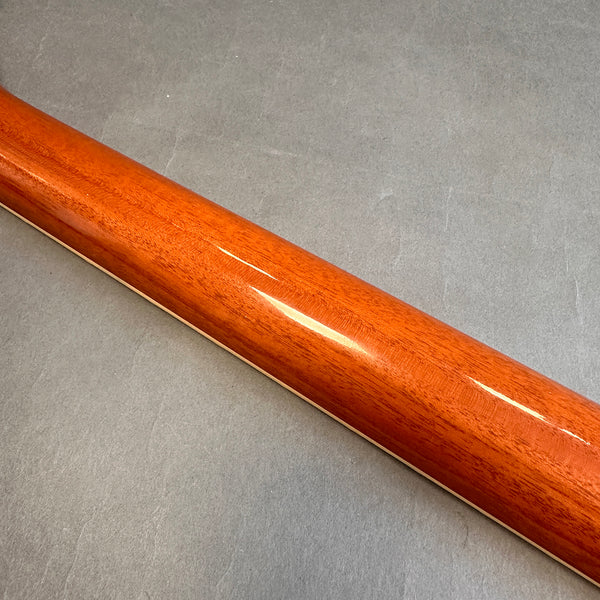 Glossy mahogany guitar neck with smooth finish on a gray background