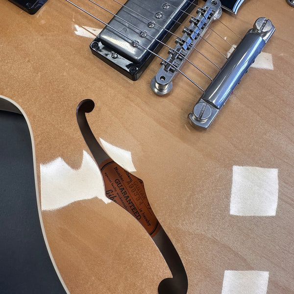 Close-up image of a natural wood finish semi-hollow electric guitar body featuring an f-hole, chrome pickup, and tailpiece hardware from Coffee House Guitars.