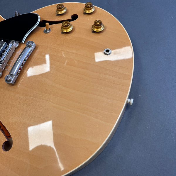 Close-up of natural finish hollow body electric guitar top with amber control knobs, chrome bridge, and black pickguard on gray background