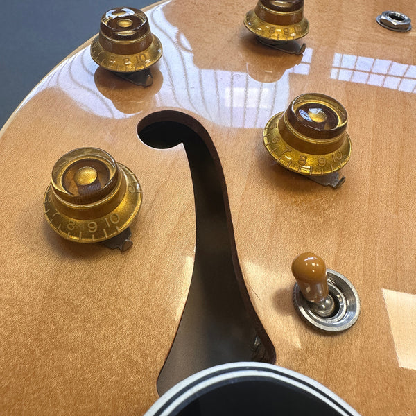 Close-up of amber tone control knobs and toggle switch on natural finish semi-hollow electric guitar with f-hole and glossy wood grain top